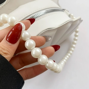 Close-up of white shell bag featuring large faux pearl handle and silver zipper detail