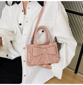 Detail of pink bow handbag featuring a heart rhinestone and pleated faux leather texture