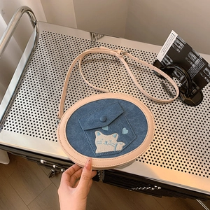 Detail showing blue denim round crossbody bag with cat embroidery and pink leather trim