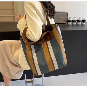 Detail view of striped canvas tote bag with leather straps and reinforced bottom corners