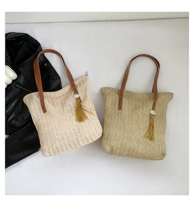 Détail de sacs cabas en paille beige et marron avec anses en cuir et pompons jaunes