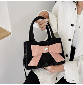 Detail of black pleated crossbody bag featuring a large pink bow with heart buckle