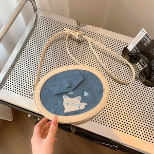 Detail of blue denim oval crossbody bag with white cat embroidery and leather strap