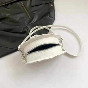 Detailed macro view of white petal-edged crossbody bag with pearl handle and metal zipper