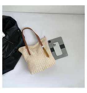 Détail d'un sac seau en paille tressée avec bandoulière en cuir brun et pompon doré