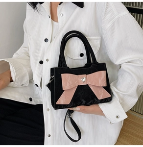 Close-up of a black box bag featuring a large pink bow and silver heart-shaped buckle