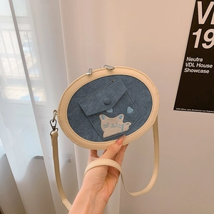 Close-up of blue denim oval crossbody bag featuring cat embroidery and cream leather piping
