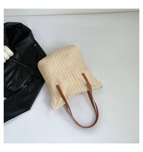 Détail d'un sac cabas en paille avec texture ondulée et anses en cuir marron