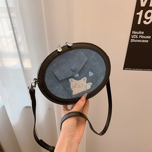 Detail of blue denim crossbody bag featuring cat embroidery and silver double zippers
