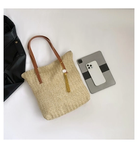 Vue détaillée du sac cabas en paille avec anses marron et un élégant pompon doré attaché