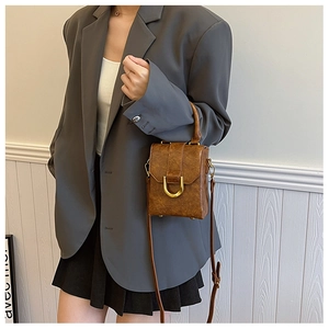 Detailed view of brown leather crossbody bag featuring a golden U-shaped metal buckle