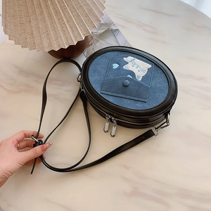 Detail of blue denim crossbody bag featuring cat embroidery and dual zipper design
