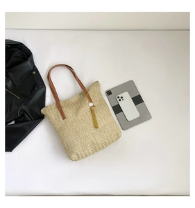 Détail d'un sac seau en paille avec bandoulières en cuir marron et pompon doré