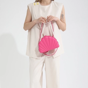 Close-up of pink shell-shaped crossbody bag with pearl handle worn by a model in beige outfit