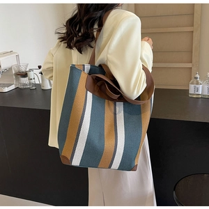Detail of canvas tote bag with yellow and navy stripes and brown leather handles in a cafe