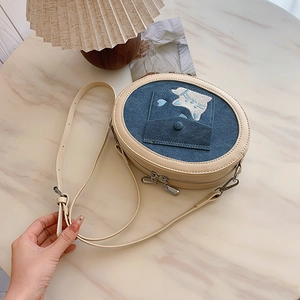 Detail of blue denim round crossbody bag with cat embroidery and white leather trim
