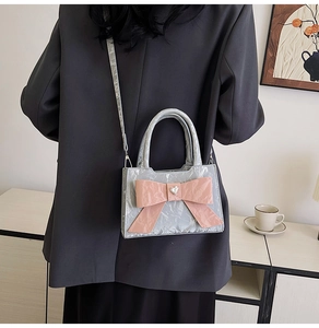 Detail of light grey handbag featuring a pink oversized bow and heart metal ornament