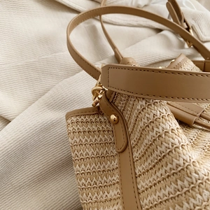 Détail macro du sac seau en paille montrant le tissage fin et la bandoulière en cuir