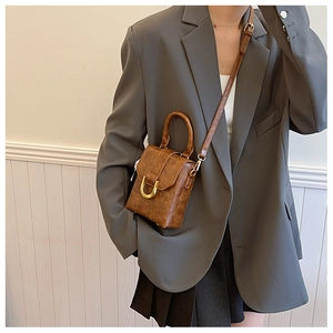 Detail of a brown mini square bag with vintage texture and golden D-shaped buckle