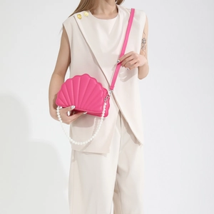Detailed view of pink shell-shaped crossbody bag with pearl strap on a fashion model