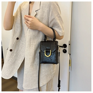 Detail of a black embossed leather mini crossbody bag with U-shaped gold metal buckle