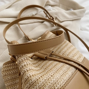 Détail d'un sac seau en paille tressée avec cordon en cuir marron et finitions dorées
