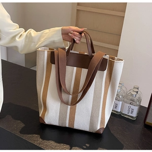 Detailed macro view of woven stripe canvas texture and brown leather trim on a tote bag