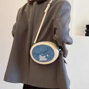 Detailed view of blue denim crossbody bag with cat embroidery worn by a model