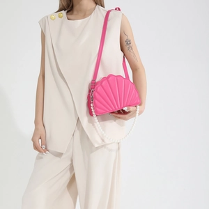 Detail view of pink shell-shaped crossbody bag with pearl strap on a minimalist model