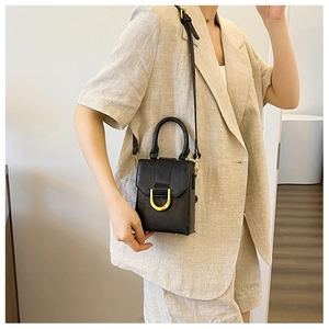Detail shot of a black croc-embossed mini handbag with a gold horseshoe buckle on a model