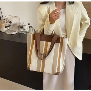 Detailed side view of a large striped canvas tote bag with brown leather handles in a cafe