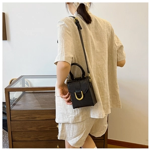 Detail of a minimalist black square mini bag with elegant gold horseshoe metal buckle