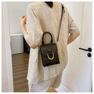 Model showing a black crossbody bag with gold D-buckle and oil-wax texture detail