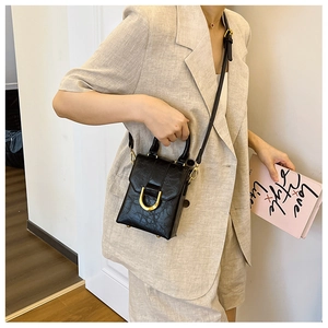 Detail of black mini crossbody bag with gold U-shaped buckle and embossed leather texture