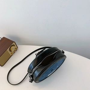 Top view of a black leather and denim oval crossbody bag with a slim strap on a table