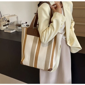 Detailed side view of the striped canvas tote bag with leather straps and reinforced corners