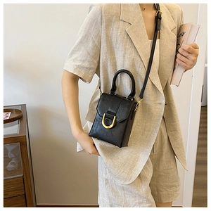 Detail of black mini crossbody bag with vintage texture and gold hardware on beige suit