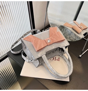 Detail of silver textured square bag featuring a large pink bow and heart rhinestone charm