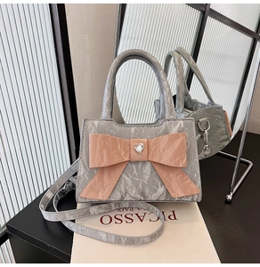 Detail of grey crossbody bag with a large pink bow and heart crystal on a desk