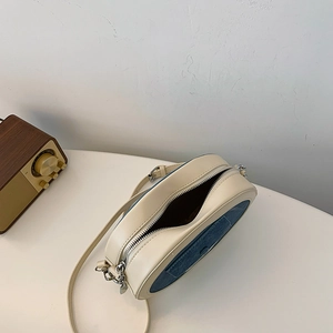 Detail view of oval crossbody bag with cream leather and blue denim patchwork design