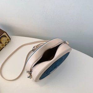 Detail view of oval crossbody bag with cream PU leather and dark blue denim stitching