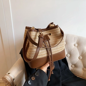 Détail d'un sac seau en paille tissée avec garniture en cuir et boucles dorées