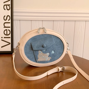 Macro view of cat embroidery on blue denim and beige faux leather crossbody bag