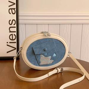Detail of a creamy white and denim blue crossbody bag featuring a cute cat embroidery