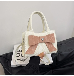Detail of creamy white pleated handbag with pink bow and heart rhinestone on a fashion book
