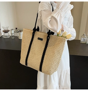 Detail of hollow woven straw tote bag featuring black rope handles and leather patch