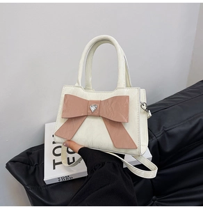 Detail of cream white handbag featuring a large pink bow and heart rhinestone accent