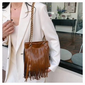 Détail d'un sac à bandoulière marron foncé avec franges et chaîne dorée au style bohème