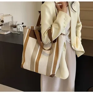 Close-up of a large striped canvas tote bag with brown straps in a modern cafe setting