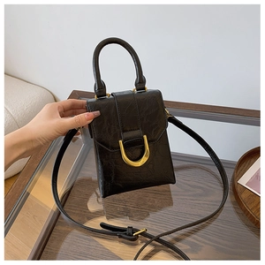 Detail view of black textured mini handbag with gold U-shaped metal buckle on a wooden tray